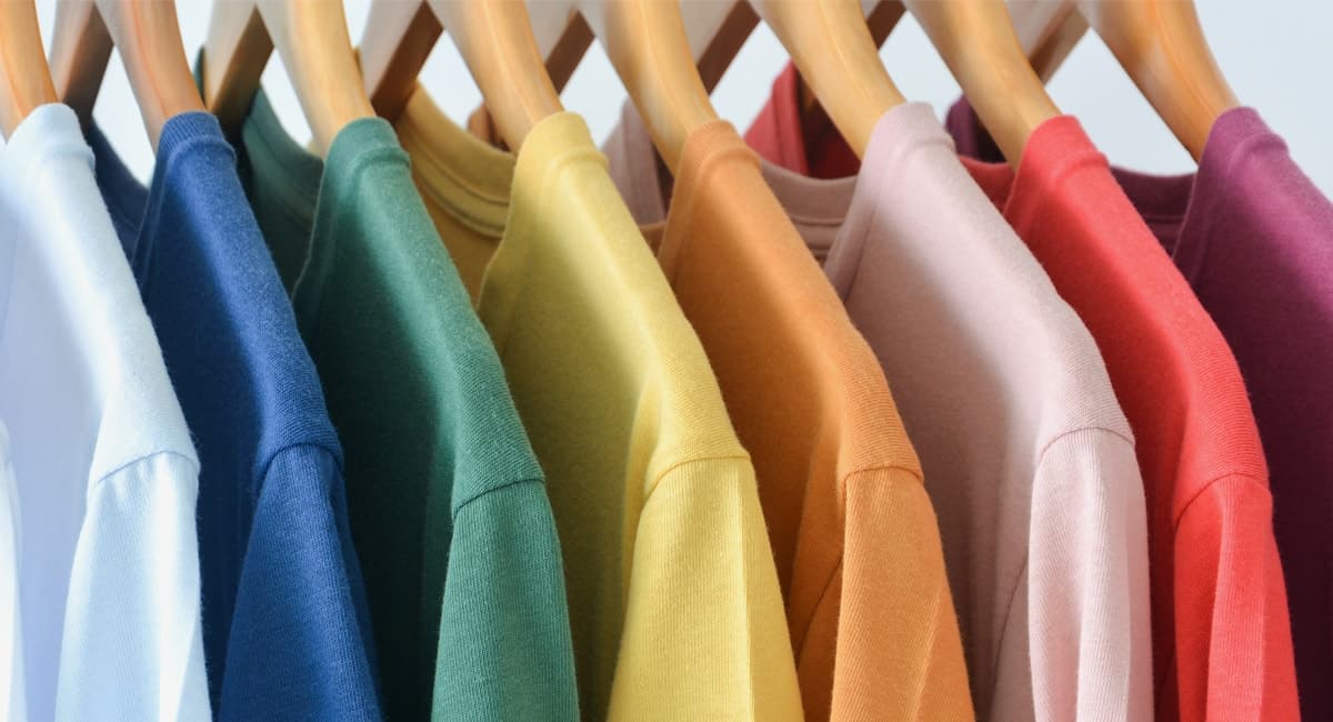 Färgglada T-shirts i regnbågens nyanser hänger i rad på trägalgar